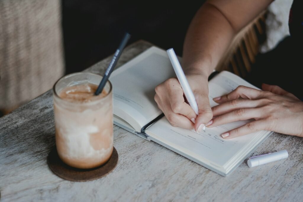 Hand writing in a journal beside a cup of coffee